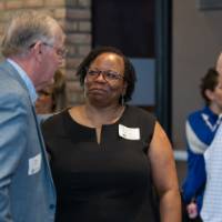 three people wearing business casual clothing chat in hallway in front of GVSU banner